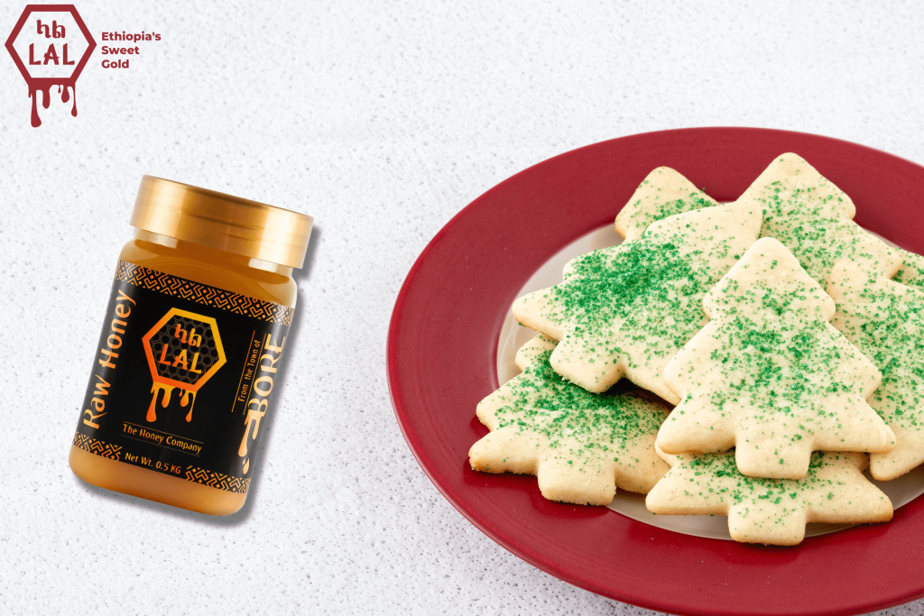 A jar of Lal's Bore White Honey beside a plate of freshly baked Christmas cookies, decorated with red and green sprinkles.